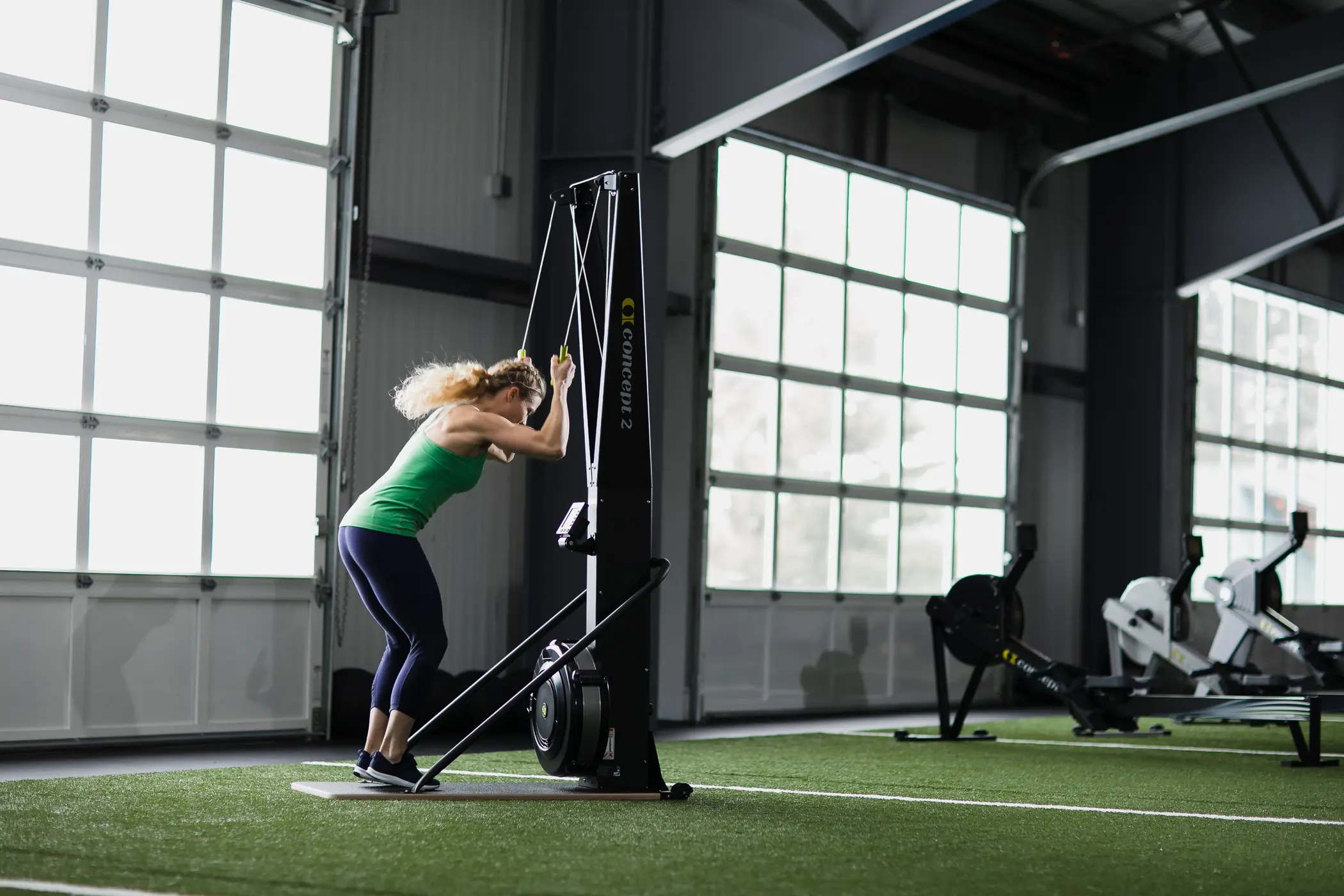 {"sl":"\u017denska v zeleni majici in temnih pajkicah izvaja vajo na vadbenem stroju v telovadnici.","hr":"","en":""}